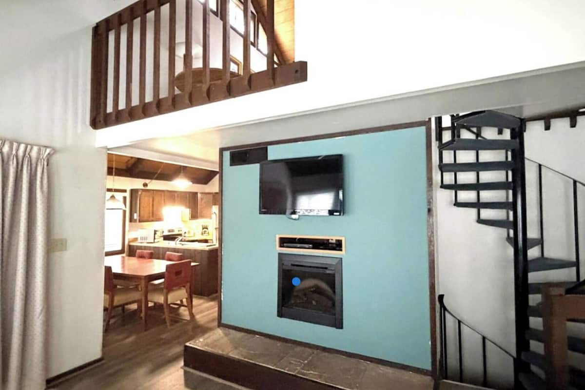 A compact kitchen with a built-in oven and microwave, a dining area with a table and chairs, and a staircase leading to an upper level.