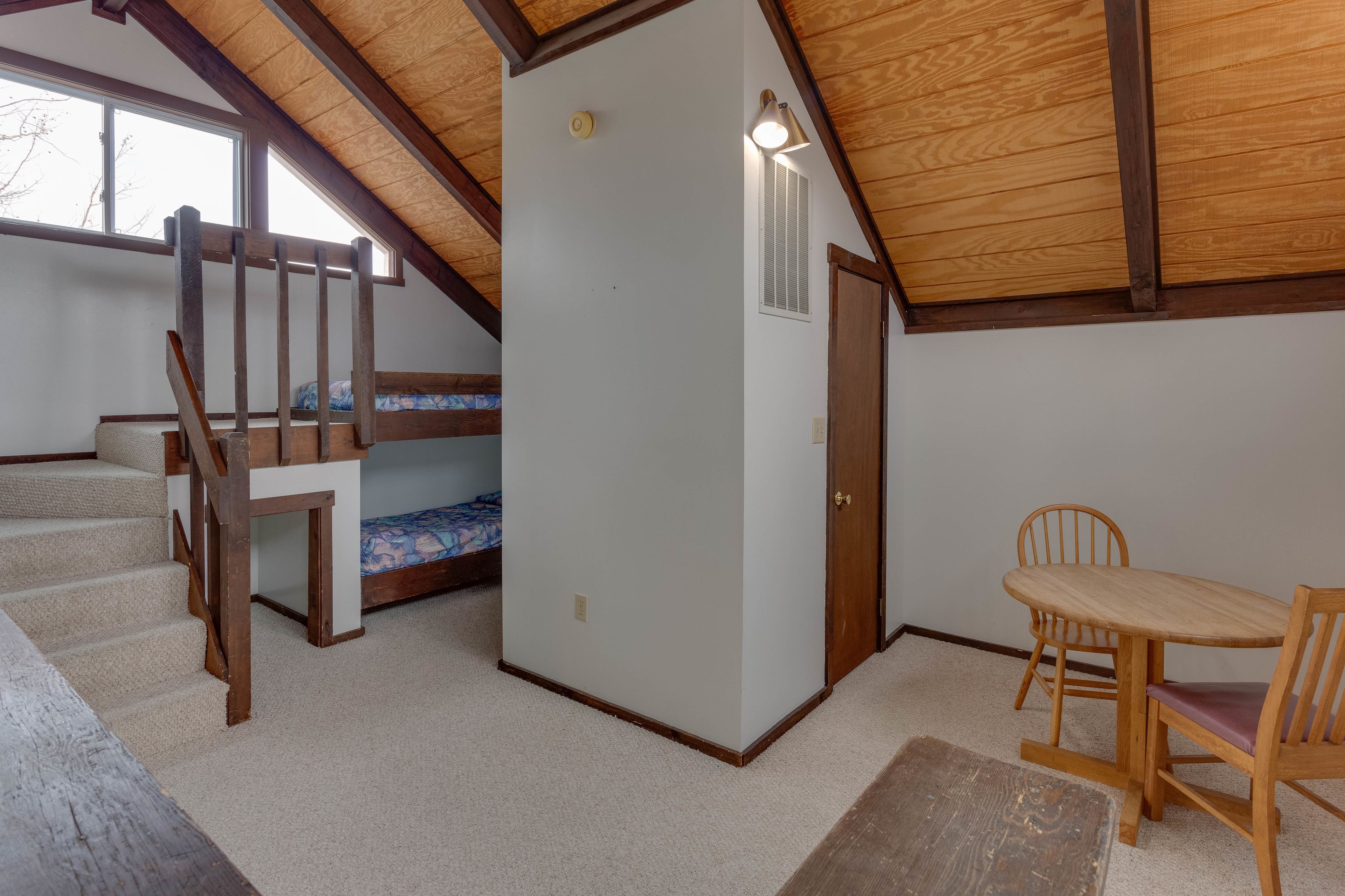 A bedroom with a bunk bed, a wooden table with chairs, a window, and a door.