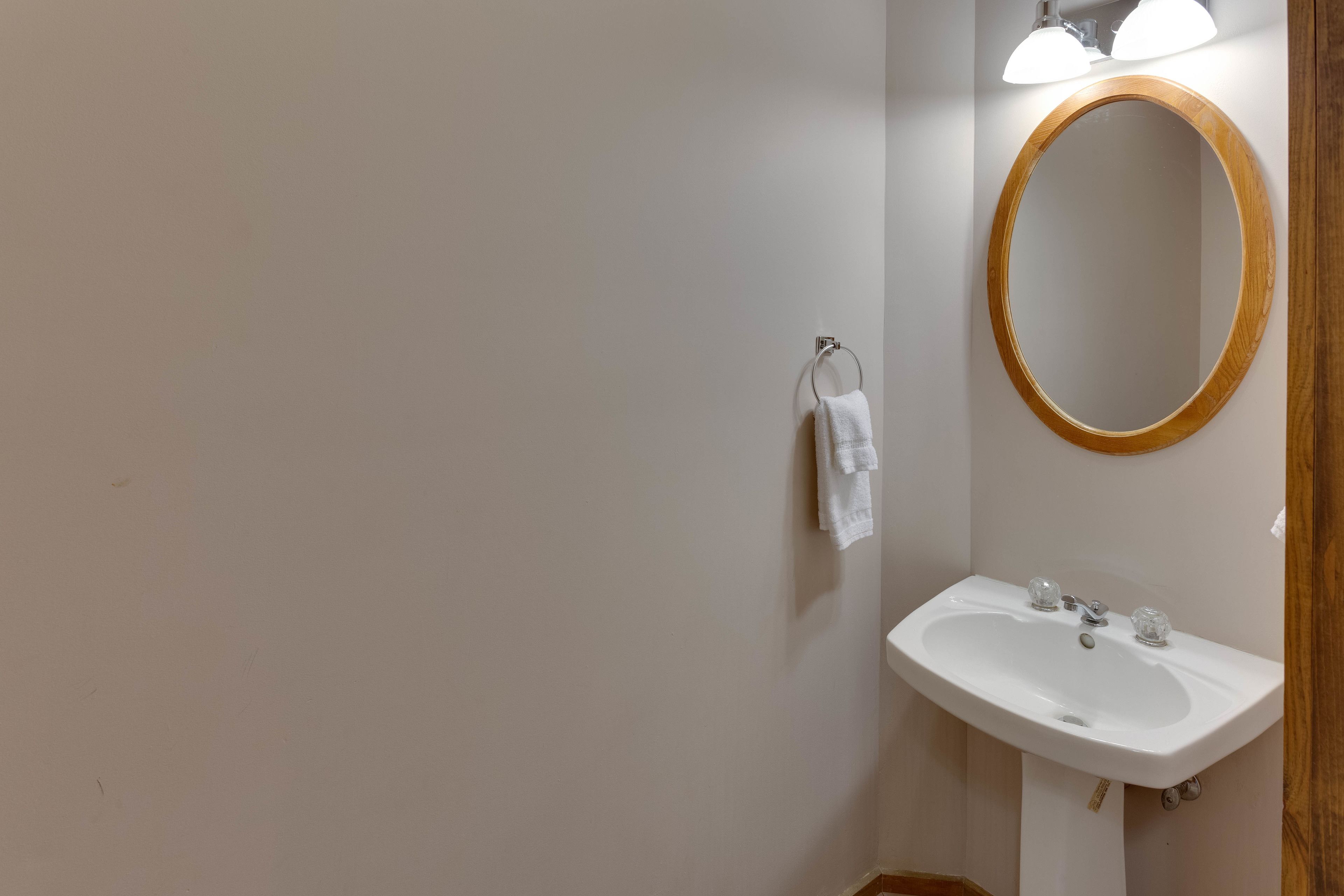 A bathroom with a white sink, a wooden-framed mirror, and a towel hanging on a metal ring.