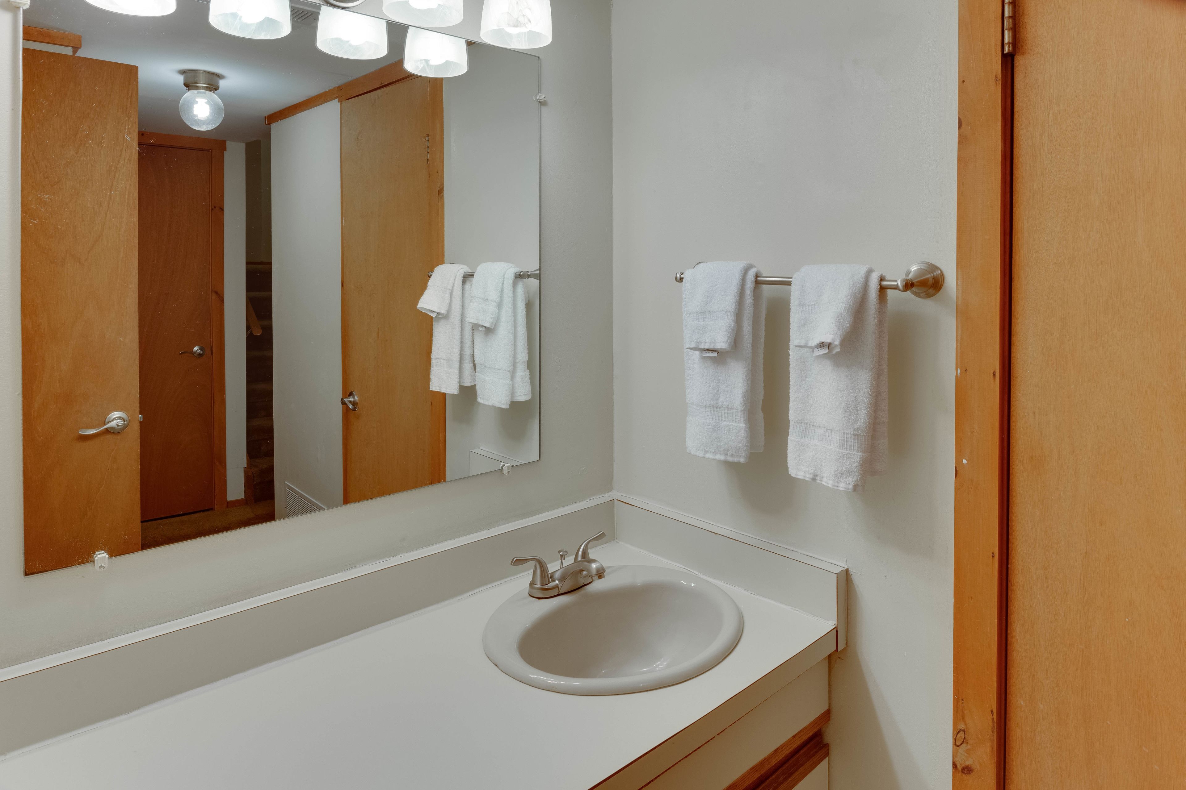 A bathroom with a white sink, a mirror, and two towel racks with white towels.