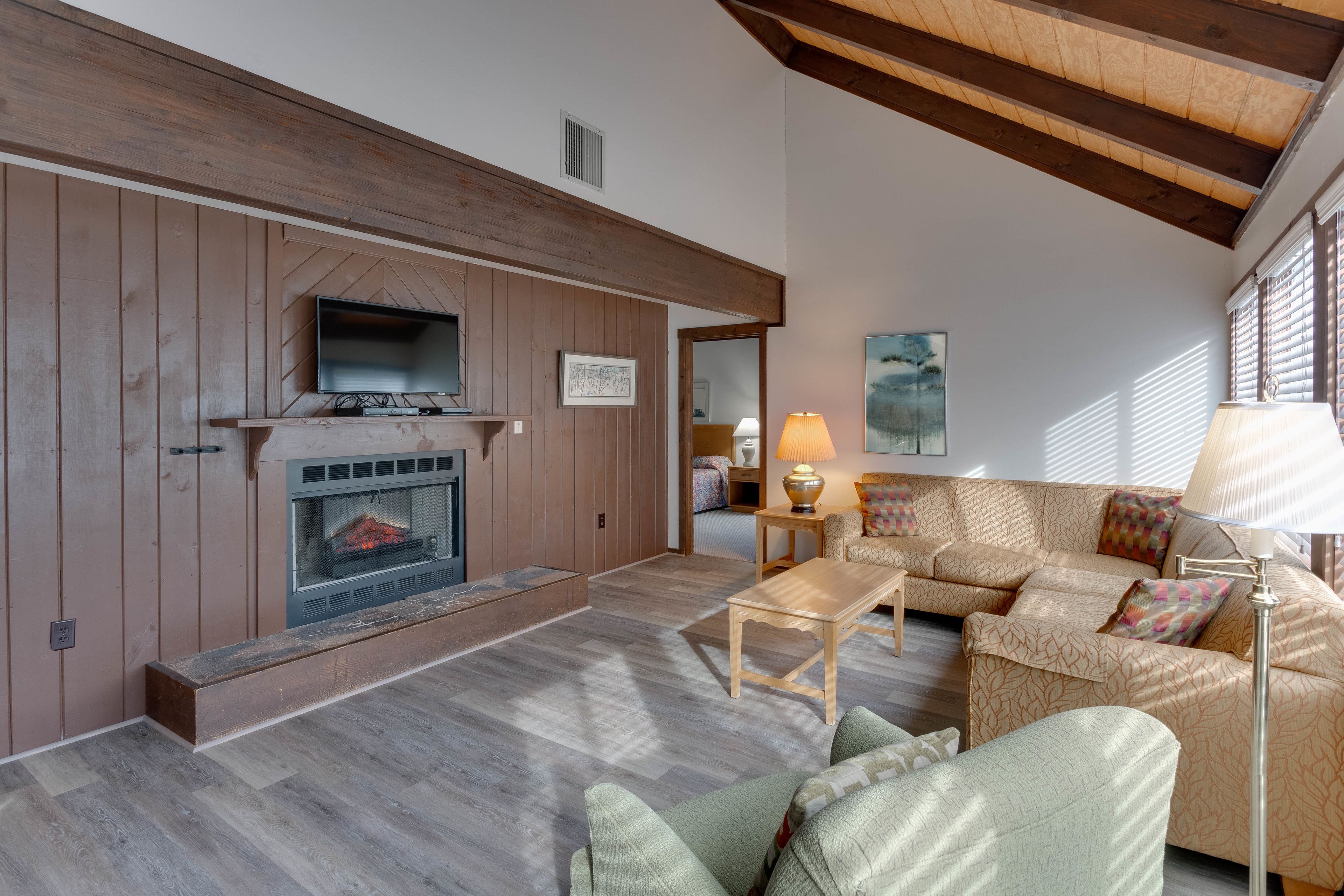 A living room with a fireplace, wooden panel walls, a sofa set, and a lamp.