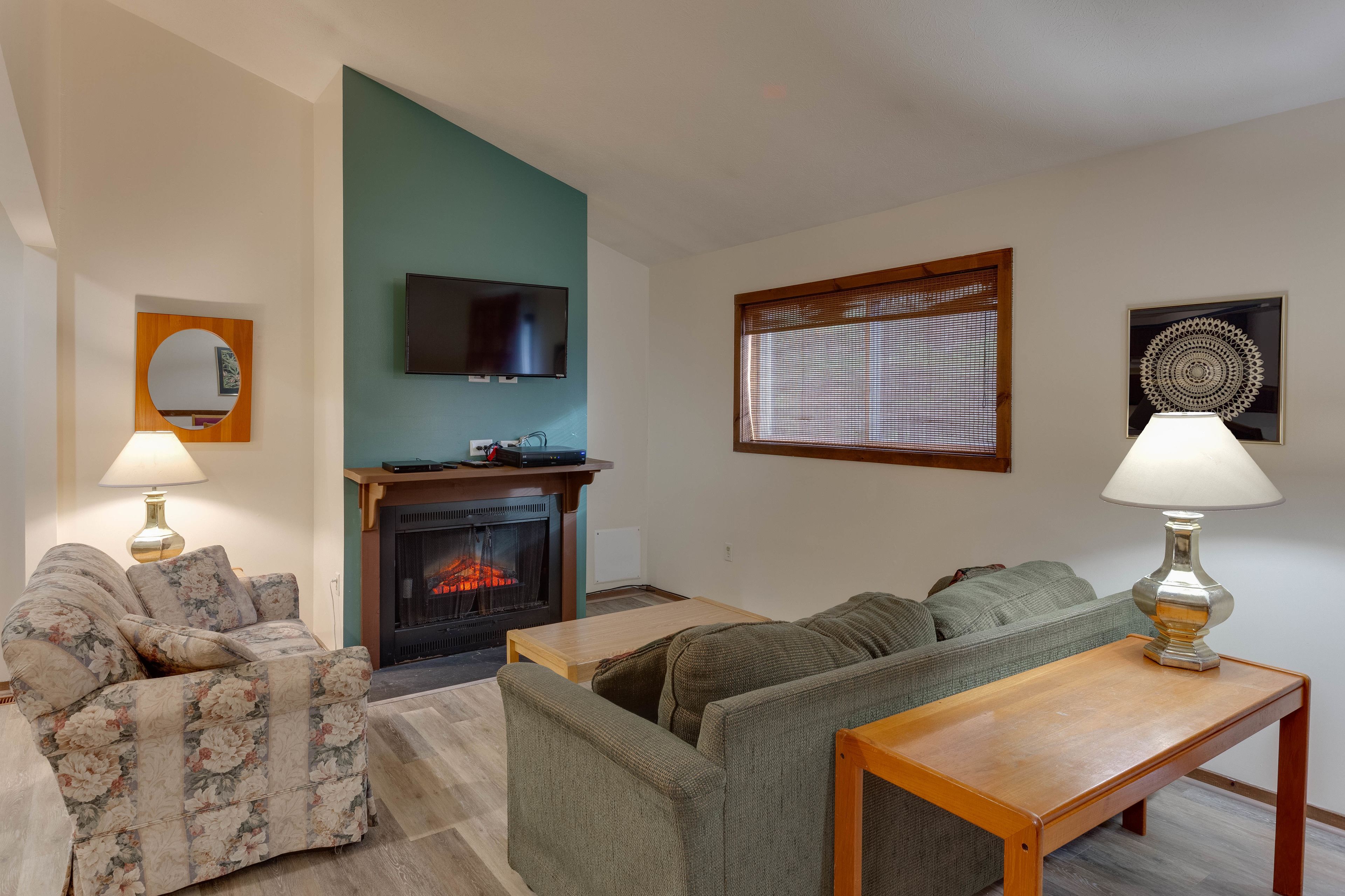 A living room with a fireplace, two sofas, a TV, and a window with blinds.