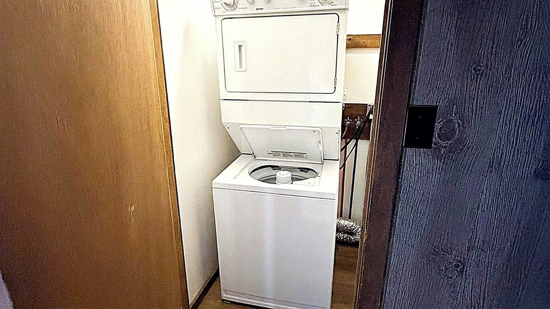 A compact laundry room with a stacked washer and dryer, a wooden door, and a metal doorbell.