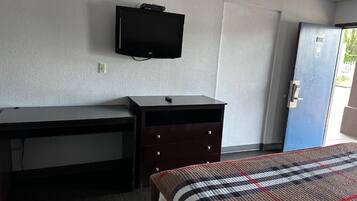 Una stanza con un letto, una scrivania, una cassettiera, un televisore e una porta.