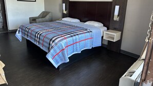 A hotel room with a large bed, a chair, a bedside table, and a wall-mounted light fixture. - Deluxe INN  Augusta (Augusta)