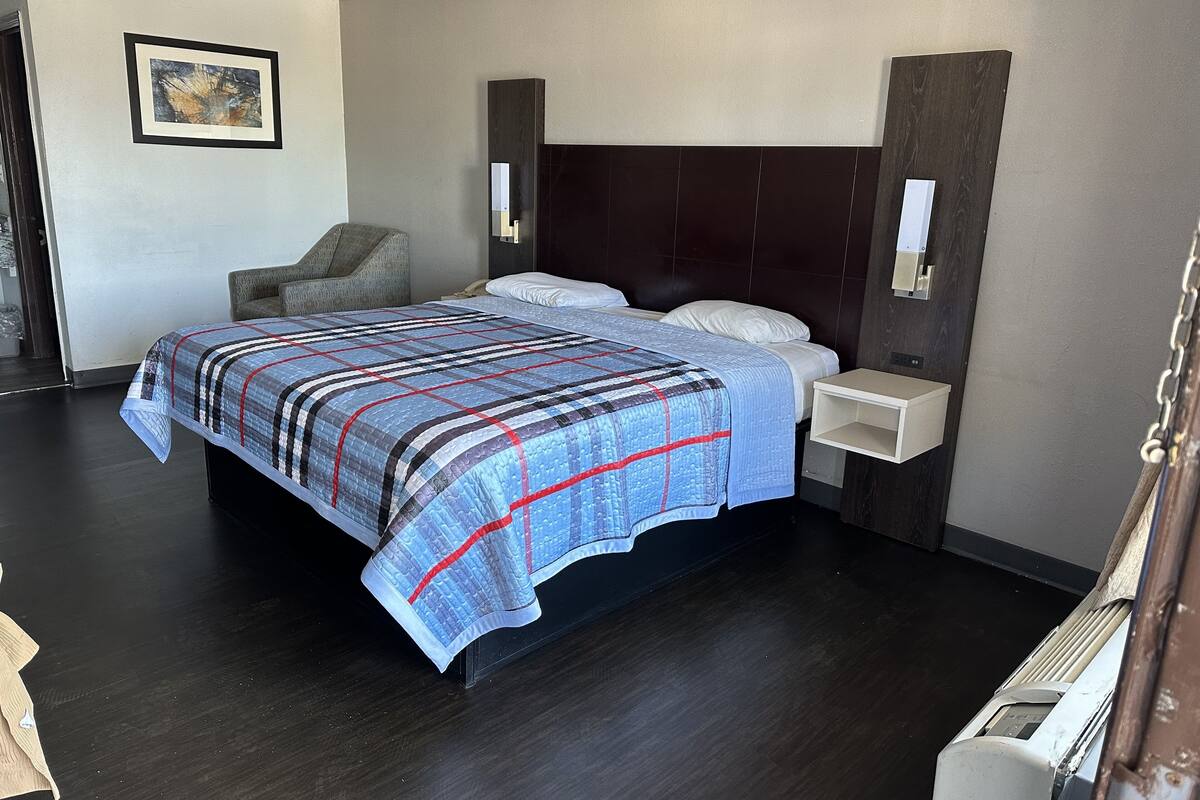 A hotel room with a large bed, a chair, a bedside table, and a wall-mounted light fixture.