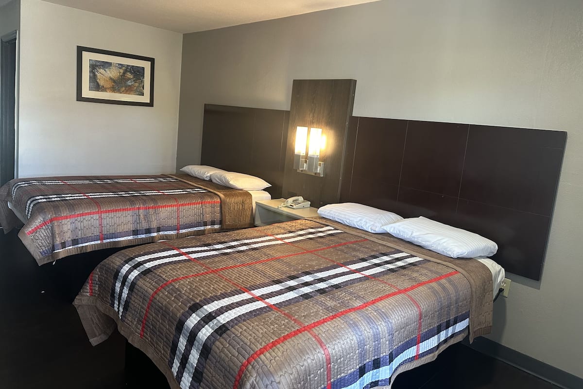 A hotel room with two beds, a nightstand, a phone, and a wall-mounted light fixture.
