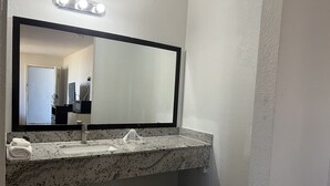 A bathroom with a granite countertop, a sink, a mirror, and a shower area. - Deluxe INN  Augusta (Augusta)