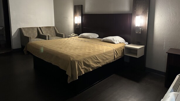 A hotel room with a large bed, a chair, a bedside table, and a wall-mounted light fixture. - Deluxe INN  Augusta (Augusta)