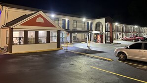 A motel with a red and white facade, a Coca-Cola vending machine, and a parking lot with a white car. - Deluxe INN  Augusta (Augusta)