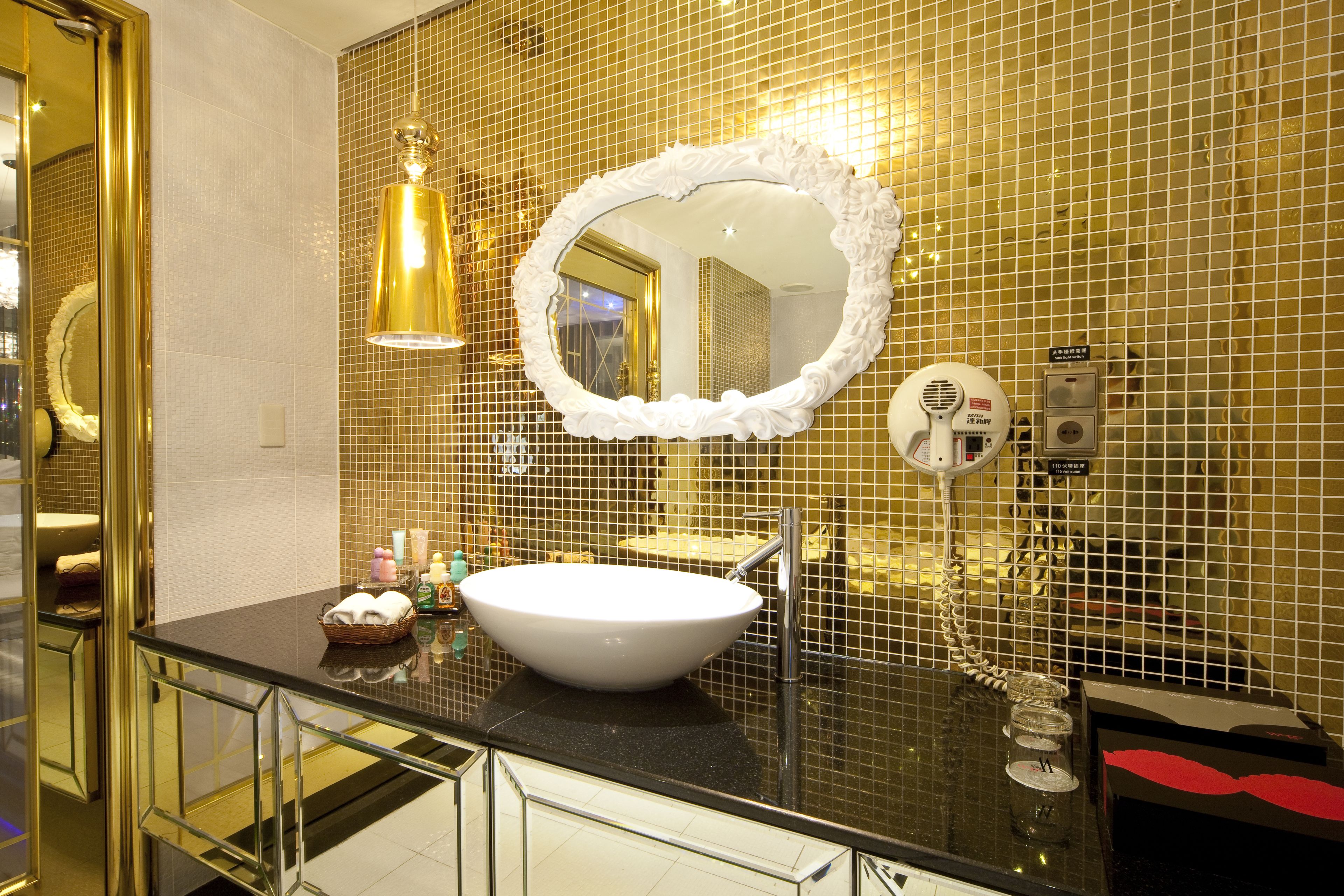 A bathroom with a white sink, gold mosaic tiles, a large mirror, and a glass railing.