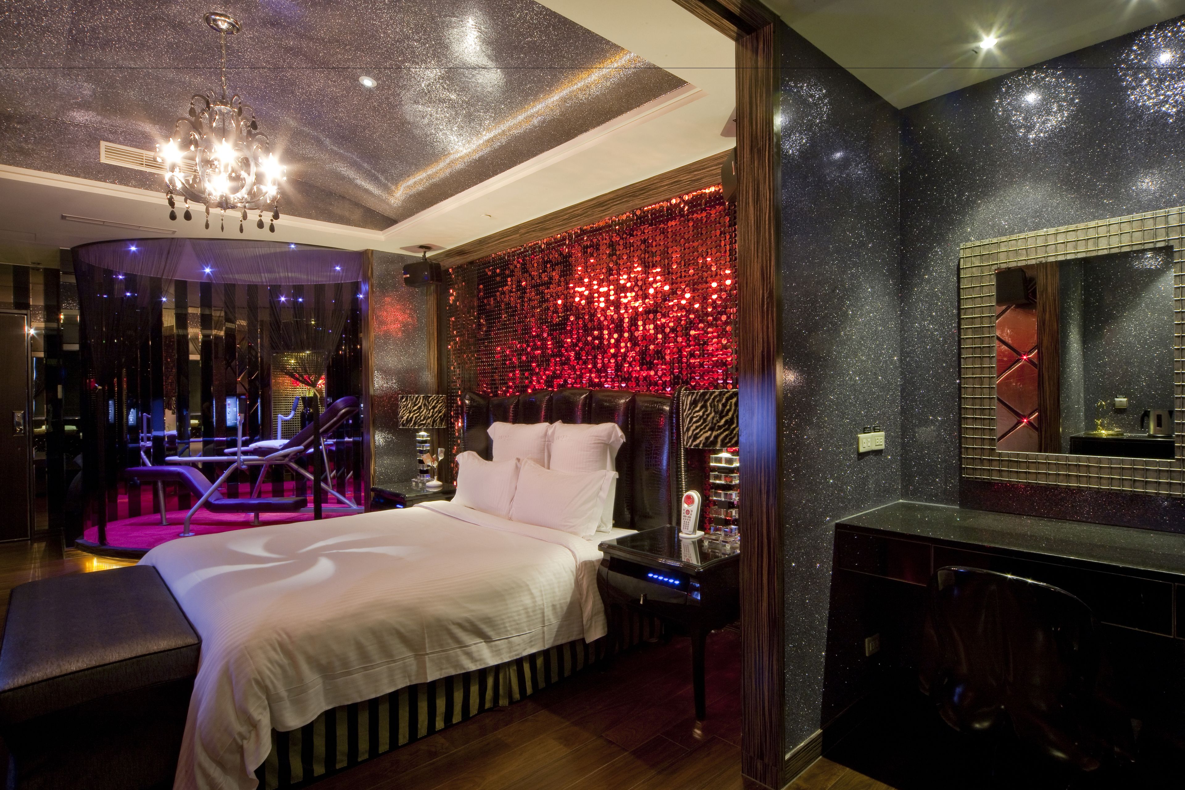 A modern bedroom with a large bed, a vanity with a mirror, and a red decorative wall.