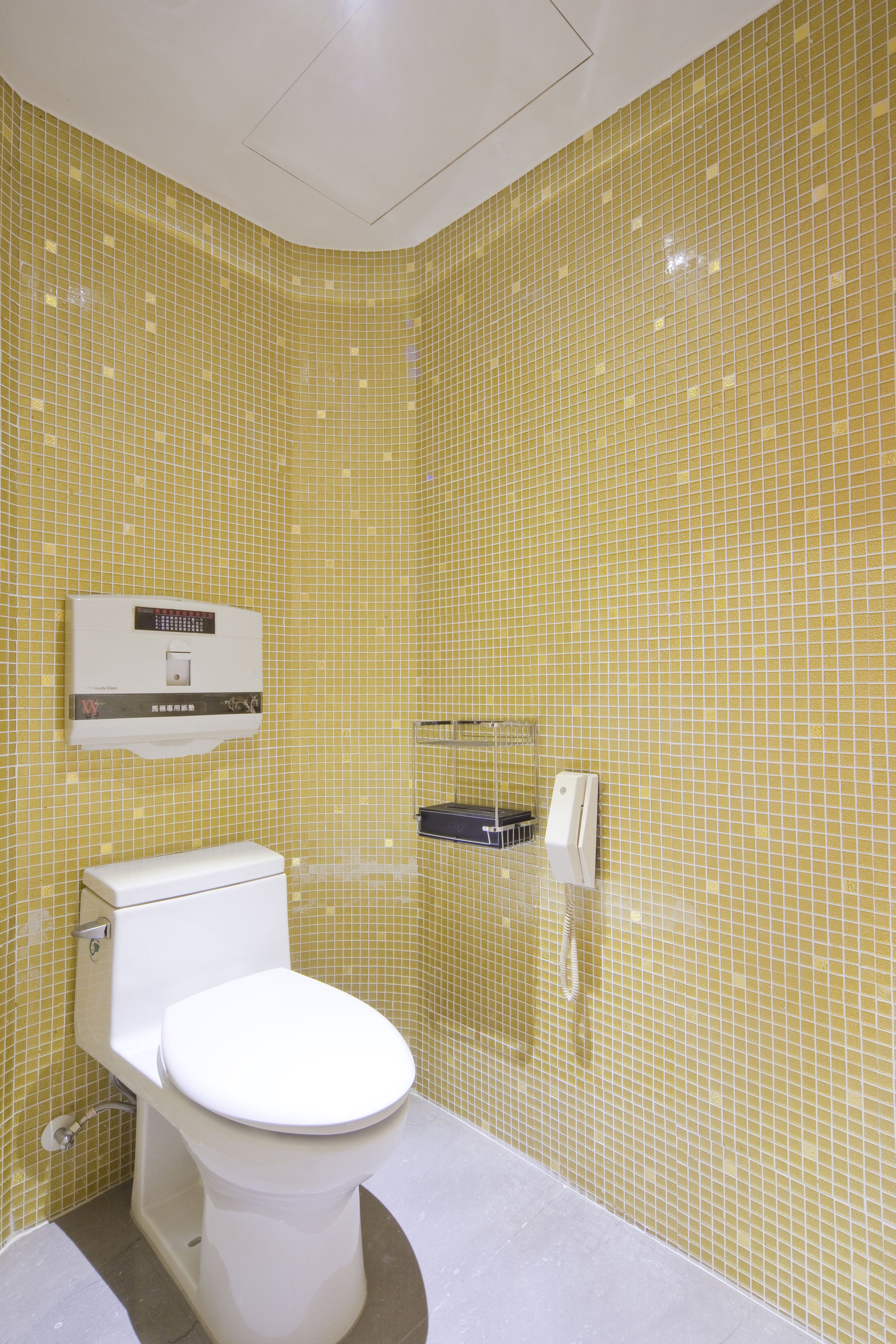 Une salle de bain avec des carreaux de mosaïque jaunes, des toilettes blanches, un sèche-mains et un chauffe-eau.