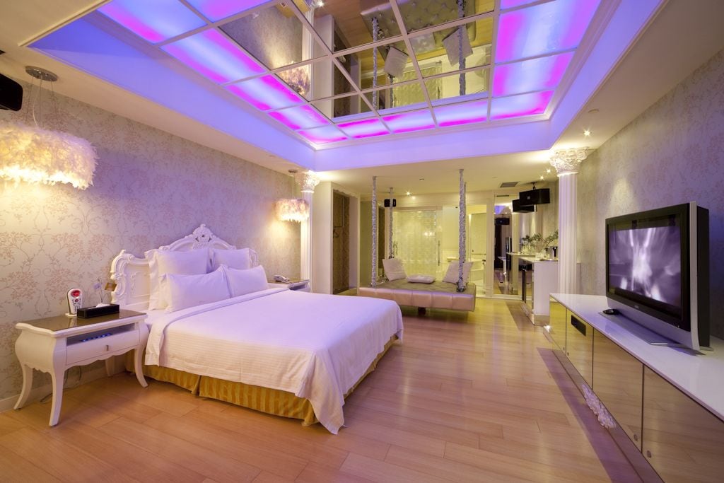 A modern hotel room with a large bed, a TV, a seating area, and a glass ceiling.
