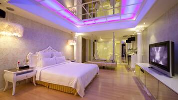 A modern hotel room with a large bed, a TV, a seating area, and a glass ceiling.