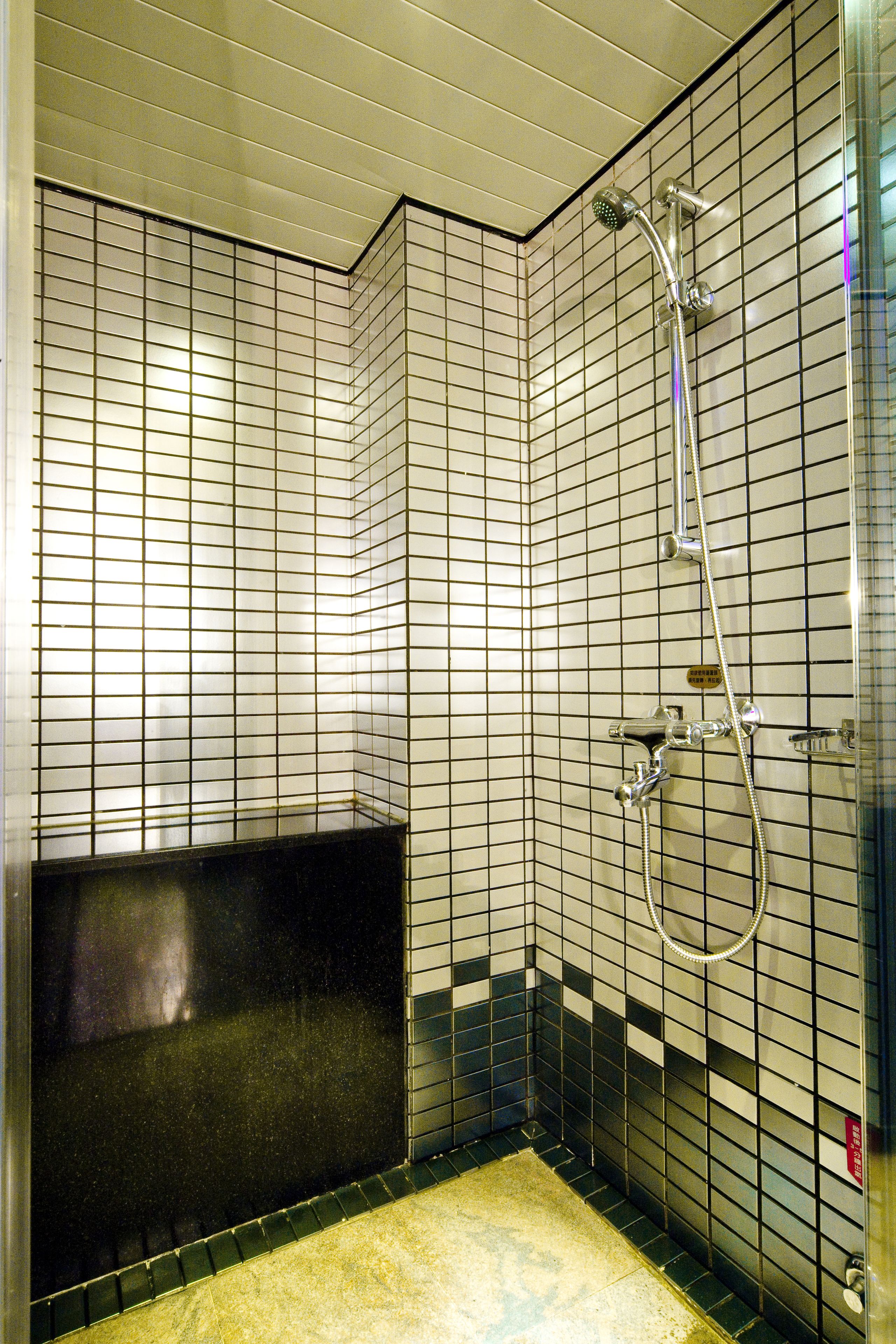 A small, tiled shower area with a handheld showerhead and a handheld shower attachment.