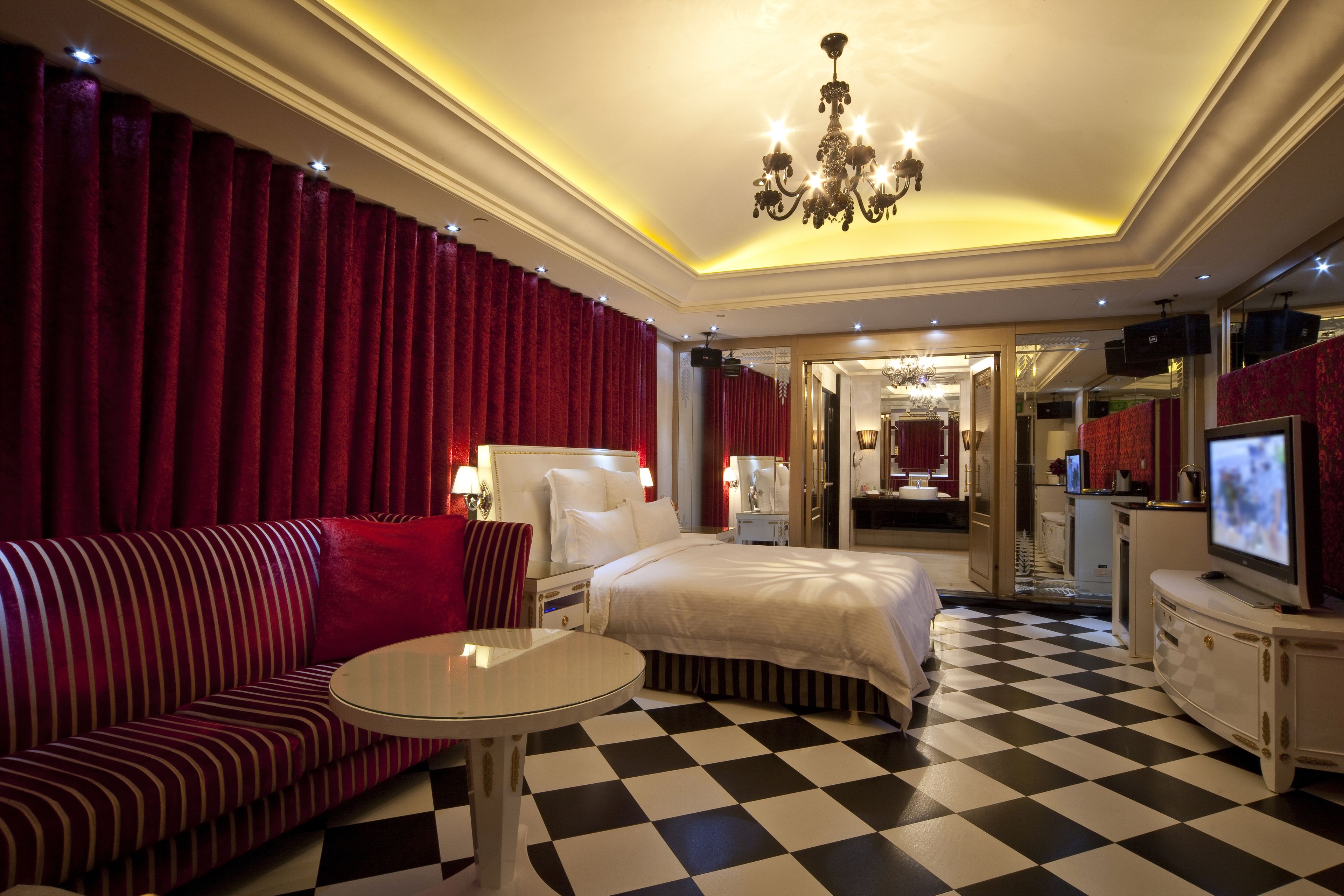 A hotel room with a checkered floor, a bed, a sofa, a TV, and a chandelier.