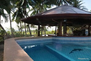 A swimming pool with a wooden pavilion, surrounded by palm trees. - Aqua-Landia Resort (Dauin)