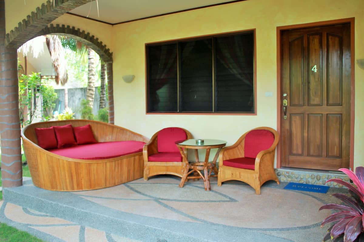 Una habitación con un sofá de madera curvado, dos sillas de madera, una mesita redonda y un ventanal grande.