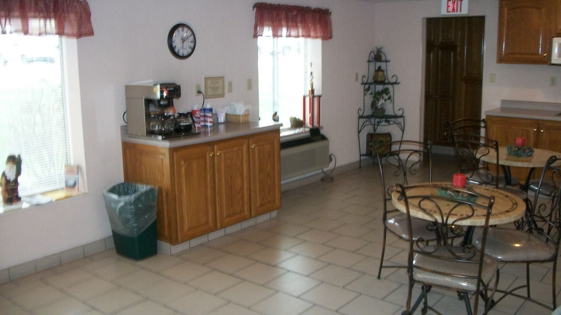 Una cocina con armarios de madera, una cafetera, un cesto de basura y un comedor con sillas de metal y una mesa.