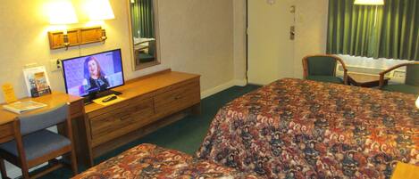 A hotel room with a bed, a desk with a computer, a chair, and a television.
