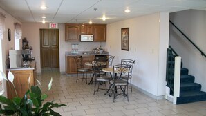 A spacious kitchen with wooden cabinets, a microwave, and a dining area with metal chairs. - Budget Host Westgate Inn (London)