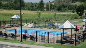 A swimming pool with lounge chairs and umbrellas, surrounded by a fence. - Budget Host Westgate Inn (London)