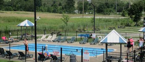 A swimming pool with lounge chairs and umbrellas, surrounded by a fence.