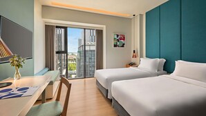 A hotel room with two beds, a desk, a chair, a TV, and a view of buildings. - Novotel Living Saigon South (Ho Chi Minh City)