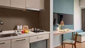 A modern kitchen with a built-in dishwasher, a sink, and a stove. There is a dining area with a table, chairs, and a sofa. A flat-screen TV is mounted on the wall.