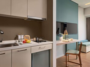 A modern kitchen with a built-in dishwasher, a sink, and a stove. There is a dining area with a table, chairs, and a sofa. A flat-screen TV is mounted on the wall.