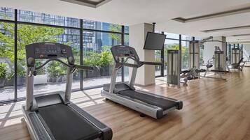 A gym with treadmills, a weight bench, and a TV screen.
