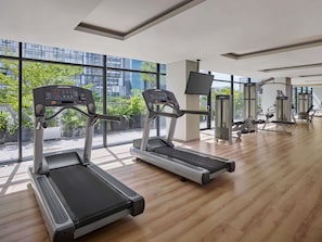 A gym with treadmills, a weight bench, and a TV screen. - Novotel Living Saigon South (Ho Chi Minh City)