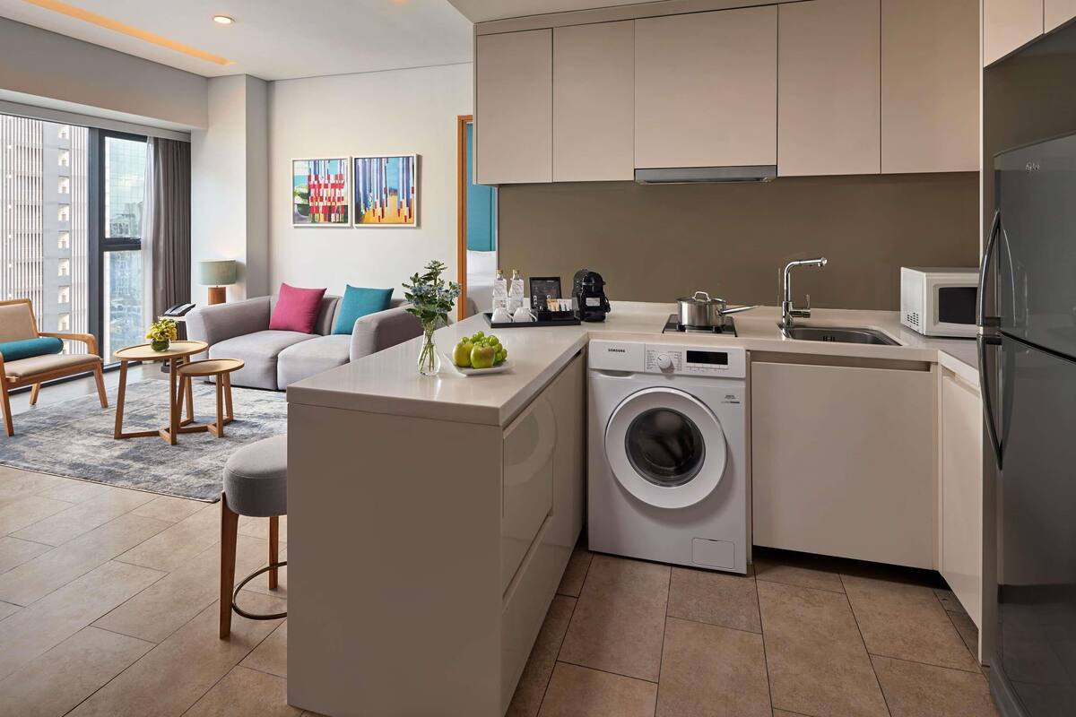 A modern kitchen with a built-in washer, a microwave, and a sink. There's a dining area with a table and chairs, and a living room with a sofa and a coffee table.