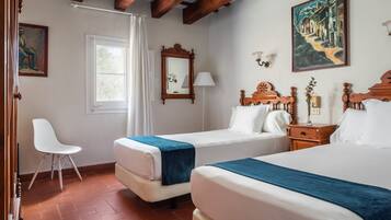 Una habitación de hotel con dos camas, un rincón de descanso con una silla, un ventanal y un cuadro en la pared.
