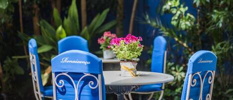 A table with a vase of pink flowers, blue chairs with "Renaivensa" embroidered on them, and a blue wall in the background.
