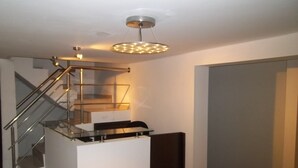 A modern staircase with glass railings and a metal handrail, leading to a landing with a black bench.
