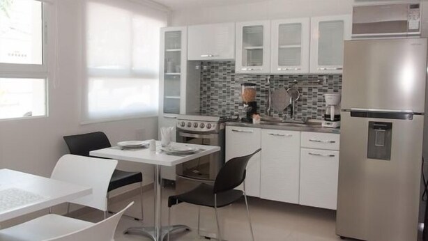 A modern kitchen with white cabinets, a stainless steel refrigerator, and a dining area with a white table and chairs.