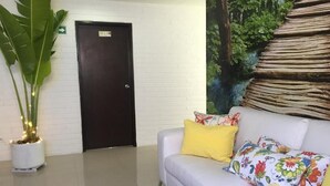 A reception area with a white couch, colorful floral cushions, a black coffee table, a potted plant, and a door with a sign.