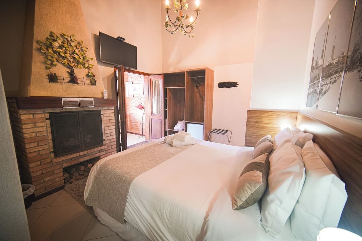 A bedroom with a fireplace, a bed with pillows, a TV, and a chandelier.