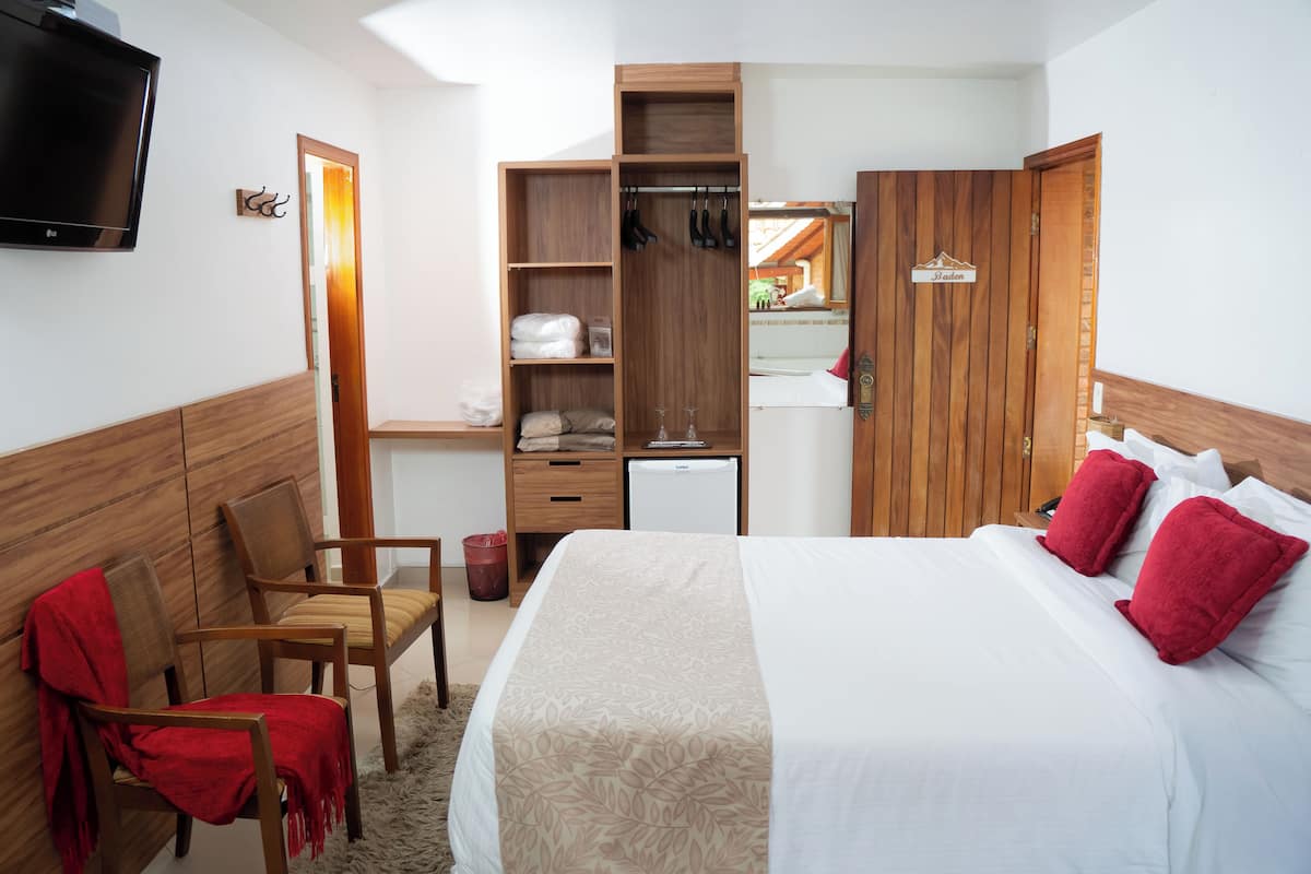 A hotel room with a bed, a TV, a wardrobe, a desk, and a chair.