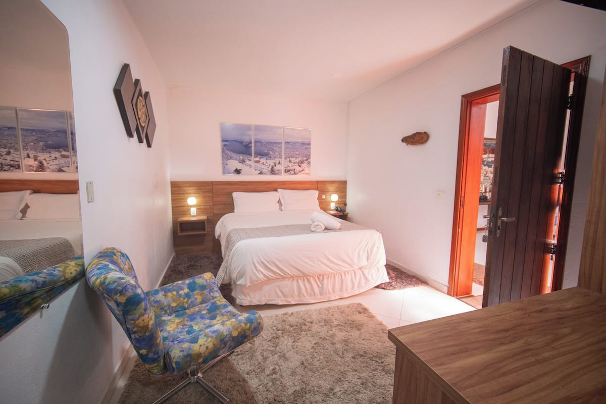 A bedroom with a bed, a chair, a wooden headboard, a rug, and a door.