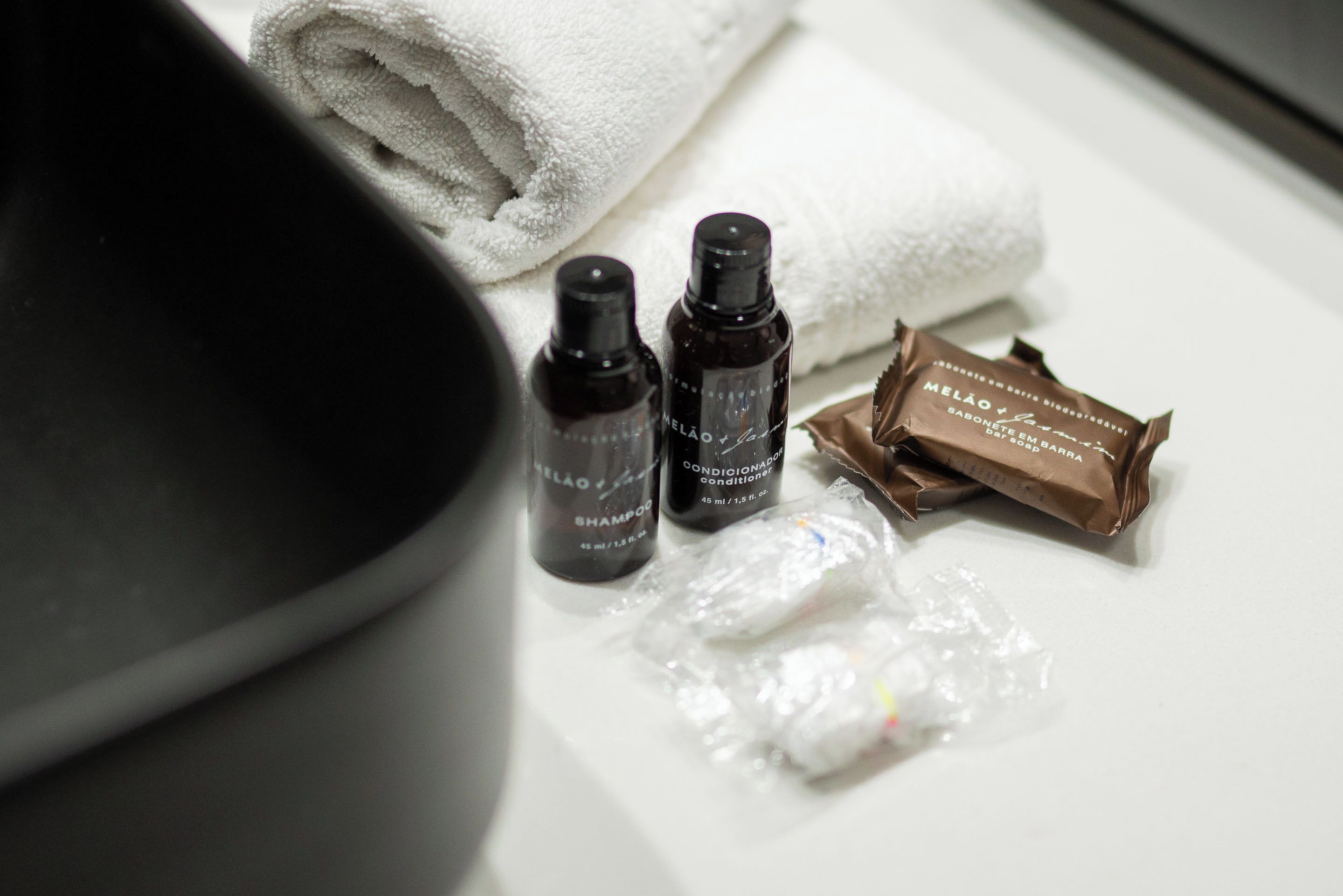 A bathroom counter with a white towel, two bottles of shampoo, a bar of soap, and a plastic bag.
