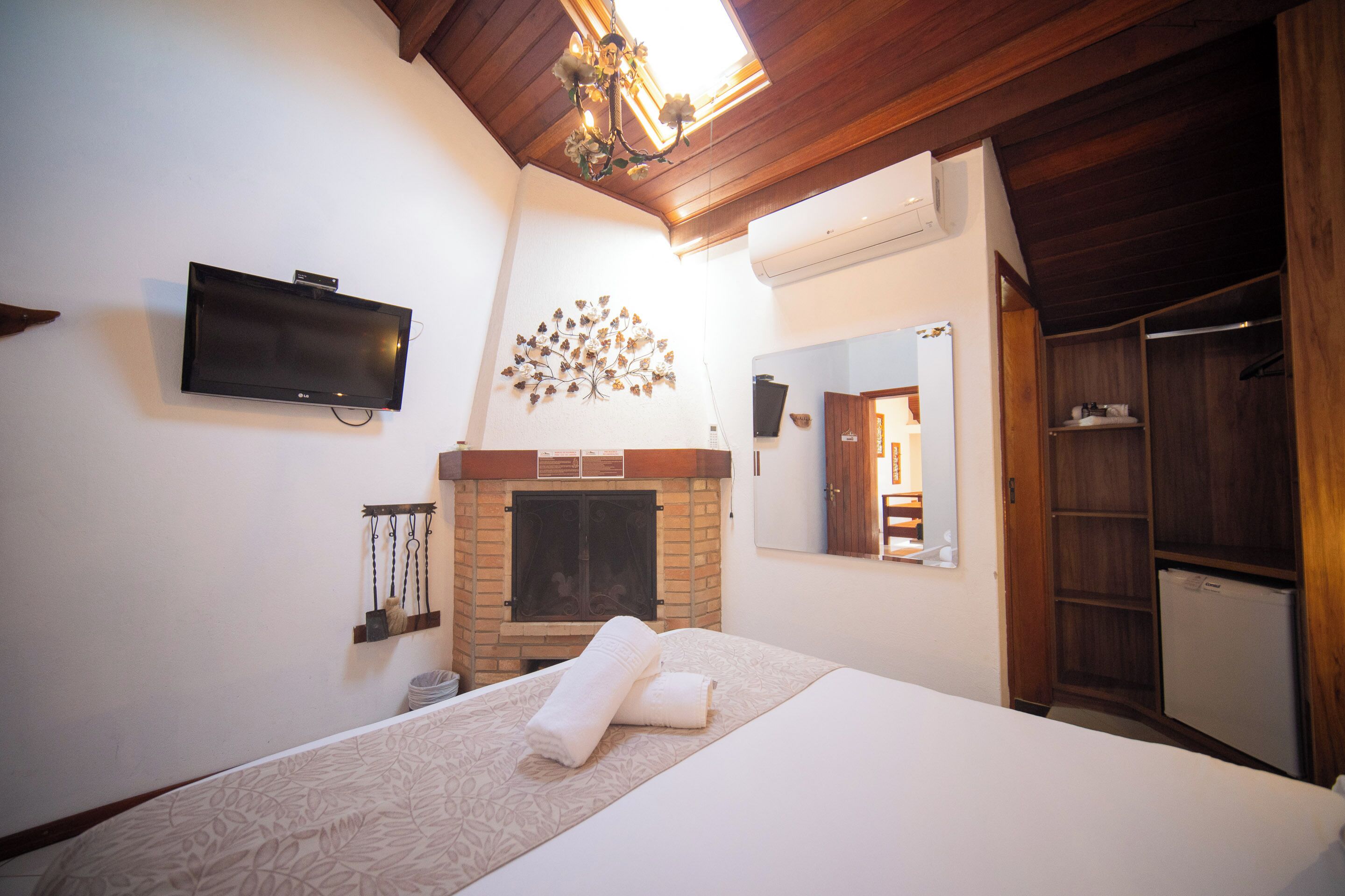 A hotel room with a bed, a flat-screen TV, a fireplace, a wardrobe, and a mirror.