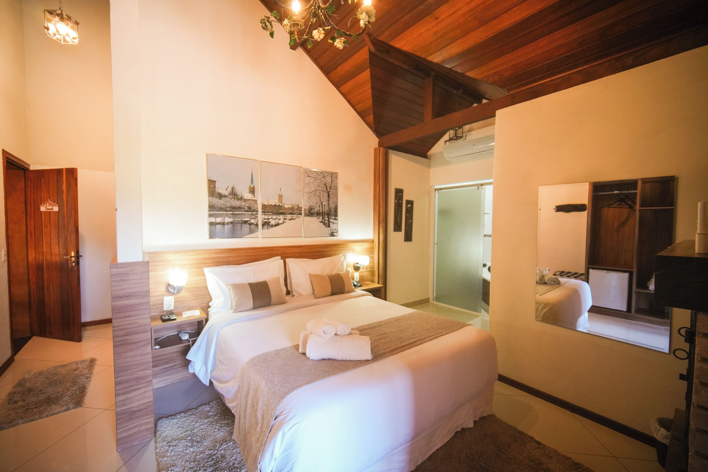 A hotel room with a large bed, bedside tables, a mirror, and a painting on the wall.