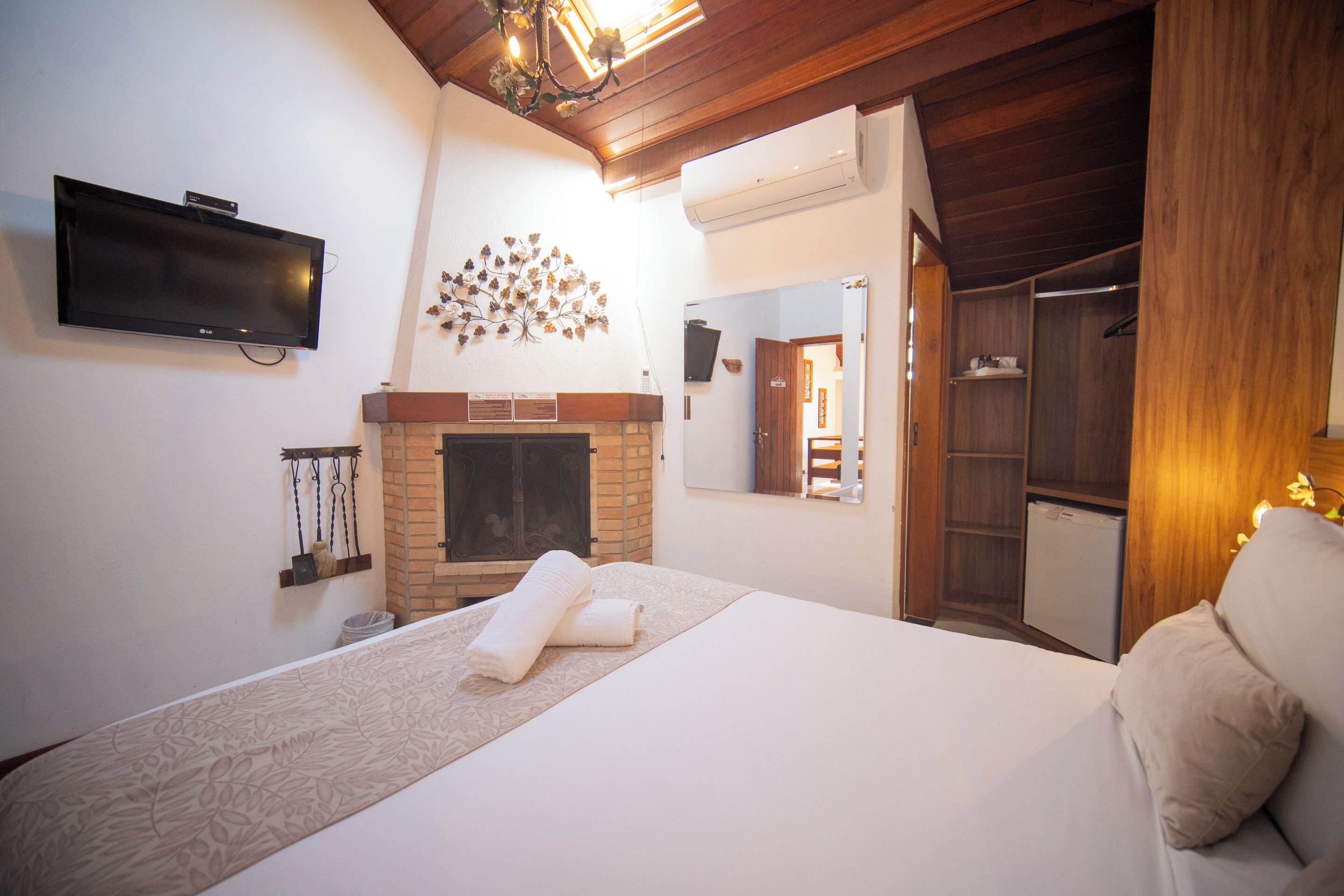 A hotel room with a bed, a flat-screen TV, a fireplace, a wardrobe, and a mirror.