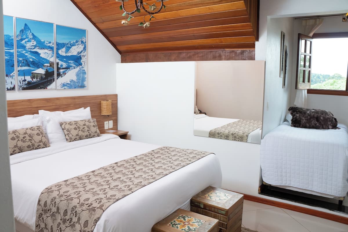 A bedroom with a wooden ceiling, a bed with patterned bedding, a nightstand, and a window with a view.