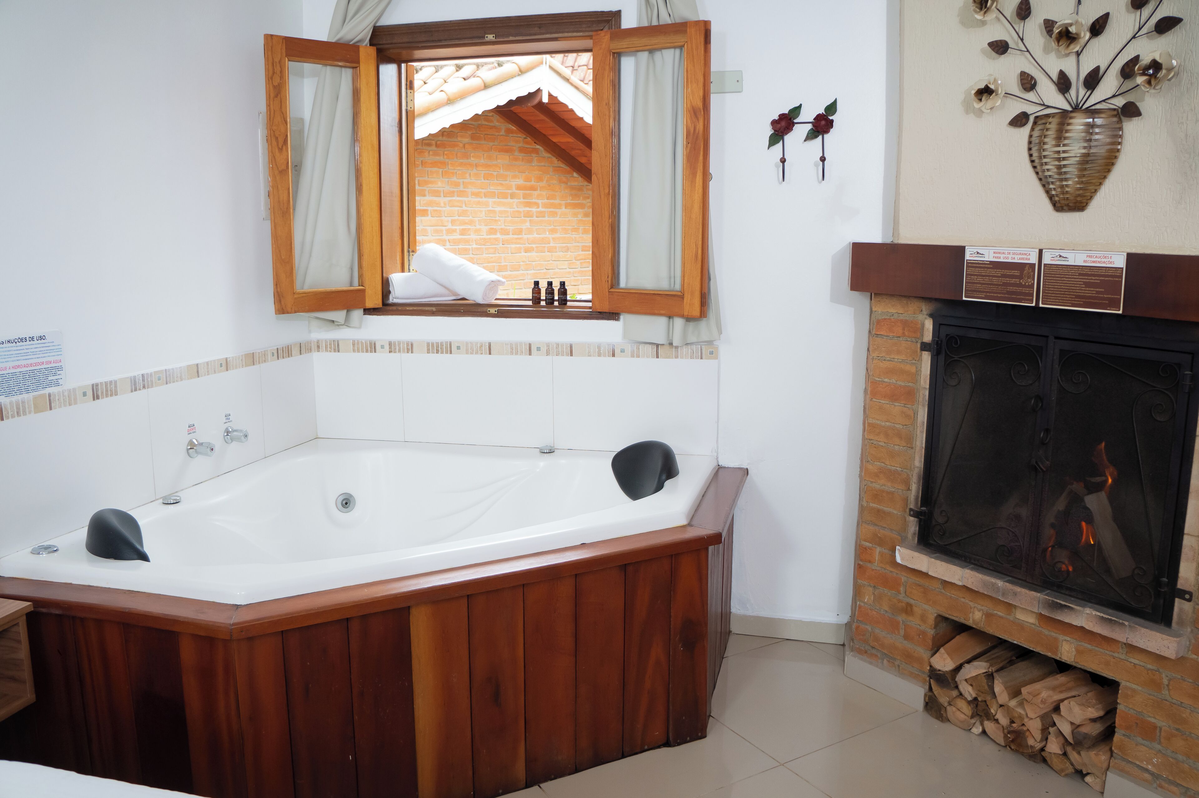 A bathroom with a wooden bathtub, a fireplace, and a mirror with curtains.