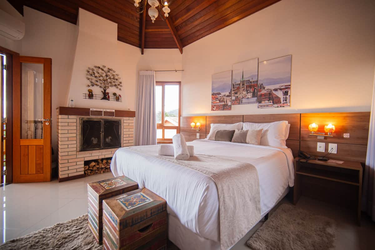 A bedroom with a large bed, a fireplace, and a cityscape painting on the wall.