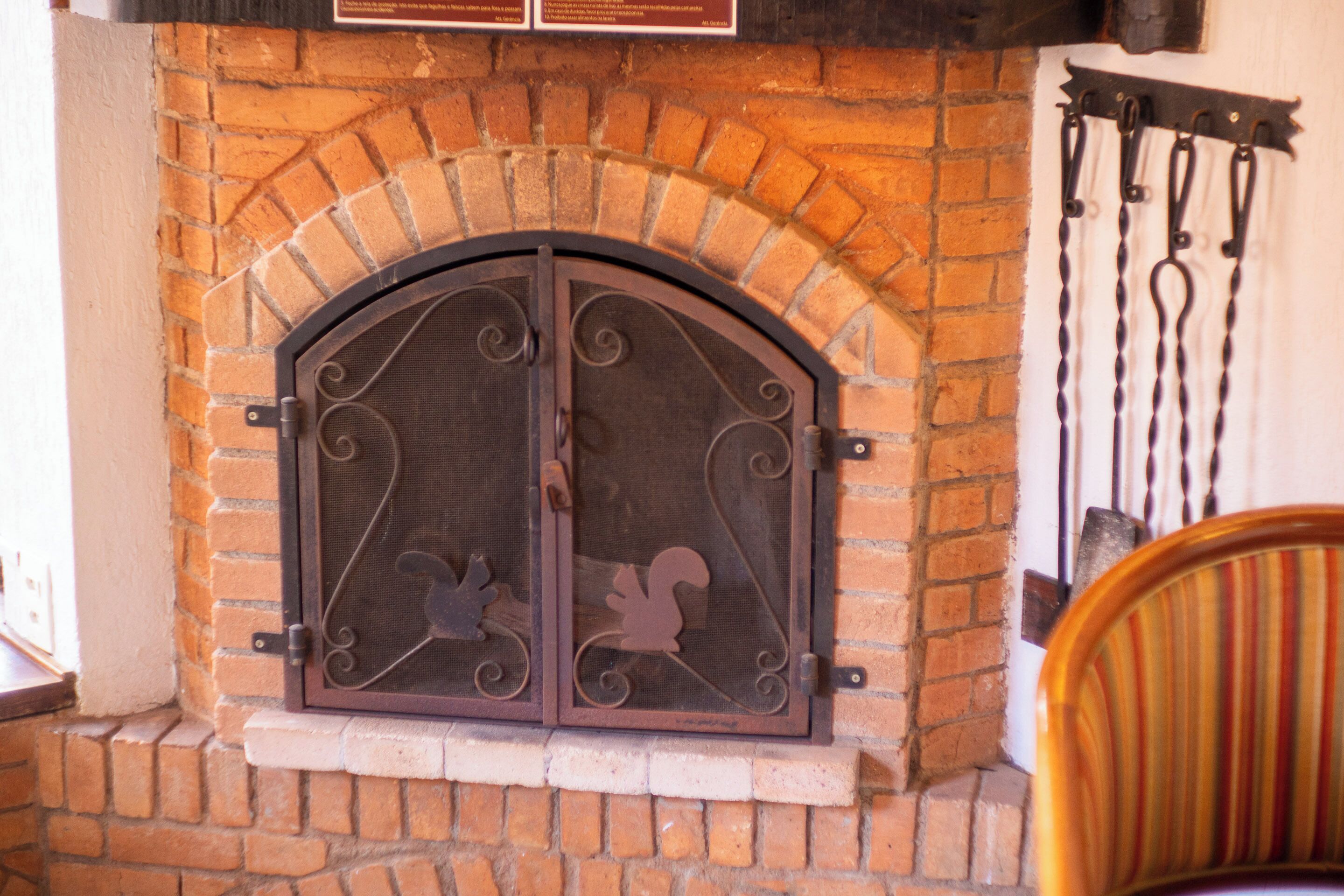 A brick fireplace with a decorative metal door and a metal curtain rod.